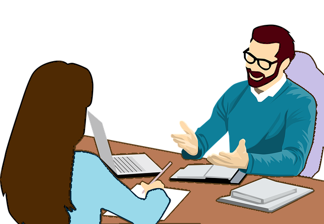 A business man and a business woman sitting opposite each other at a desk talking to each other. 