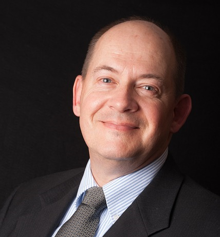 headshot photo of a smiling middle aged man in a suit and tie